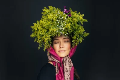 Sur un fond noir, une femme aux yeux fermés avec un chapeau floral et un foulard autour du visage