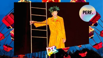 Une femme déguisée en clown avec un long manteau jaune et une perruque, une main sur une échelle