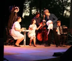 Photo de scène d'un spectacle où un groupe de comédiens et comédiennes habillées en style année 40 chantent et jouent