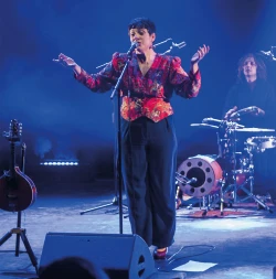 Une femme sur une scène musicale au fond bleu chante devant un micro