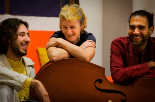 Deux jeunes homme et une jeune femme sont assis autour d'une contrebasse dans une atmosphère conviviale