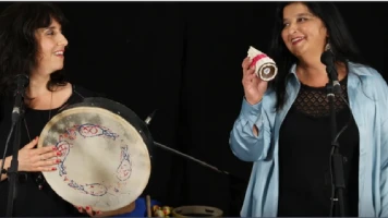 Sur un fond noir, deux femmes sont en train de jouer des percussions avec un air complice