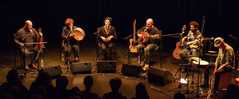 Six musiciens disposés en arc de cercle sur scène, en train de jouer