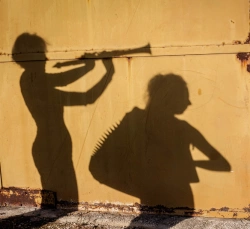 Deux ombres portées sur un mur jaune sont en train de jouer de la musique